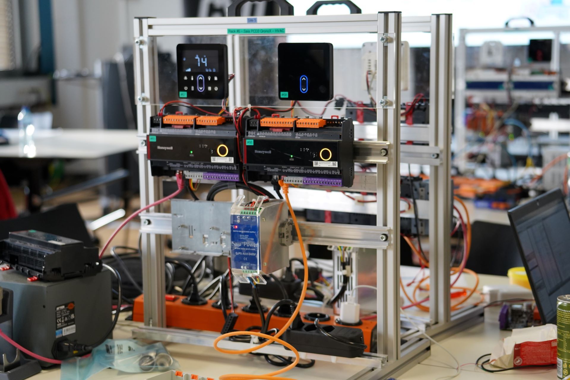 Dieses Bild zeigt eine komplexe Struktur für das Testen von Gebäudeautomation, die für Forschungszwecke oder Hackathons ausgelegt ist. Die abgebildeten Hauptkomponenten sind Feldgeräte und Regler im Zusammenhang mit HVAC-Systemen (Heizung, Lüftung und Klimatechnik), die zur Gebäudeautomations- und Steuerungsinfrastruktur gehören