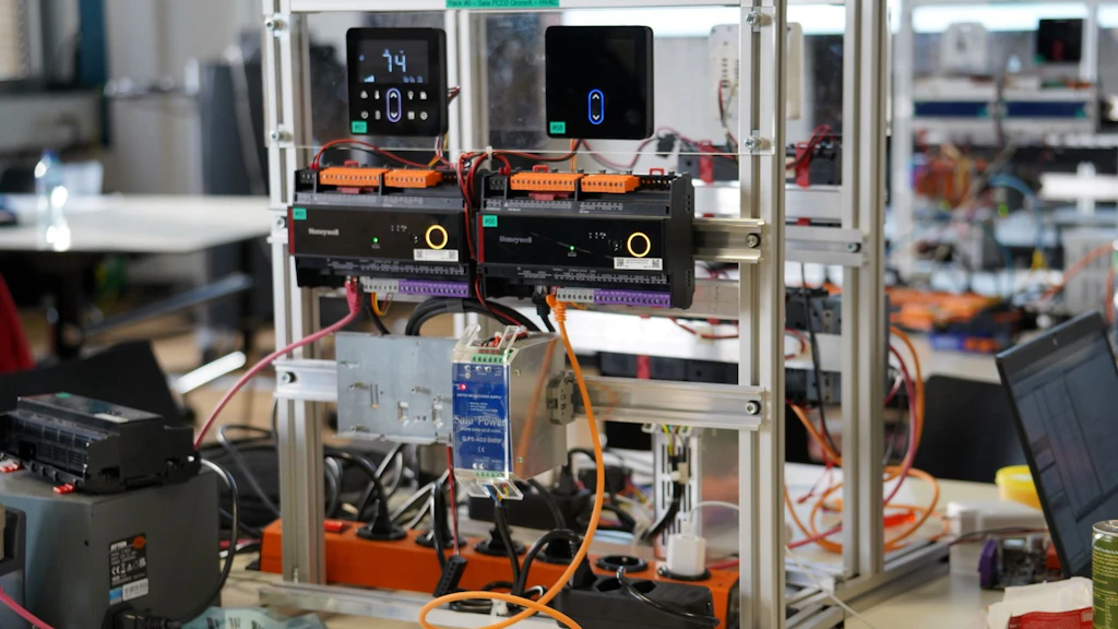 Dieses Bild zeigt eine komplexe Struktur für das Testen von Gebäudeautomation, die für Forschungszwecke oder Hackathons ausgelegt ist. Die abgebildeten Hauptkomponenten sind Feldgeräte und Regler im Zusammenhang mit HVAC-Systemen (Heizung, Lüftung und Klimatechnik), die zur Gebäudeautomations- und Steuerungsinfrastruktur gehören
